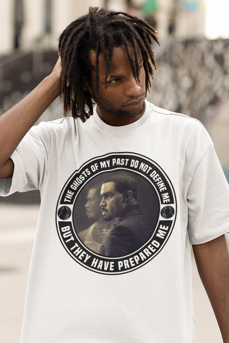 May include: White t-shirt with a black and white circular graphic featuring a man's face and the text "The Ghosts of My Past Do Not Define Me But They Have Prepared Me."