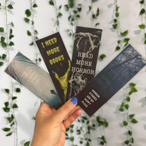 Puede incluir: Cuatro marcapáginas rectangulares con temas oscuros. Uno muestra 'I NEED MORE BOOKS' con una garra verde, otro 'READ MORE HORROR' con imágenes esqueléticas, uno dice 'HORROR STORIES ARE MY HAPPY PLACE' y el último 'THERE IS A STRANGE COMFORT IN BEING ALONE'.
