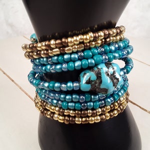 May include: A stack of turquoise and gold beaded bracelets with a turquoise stone charm.