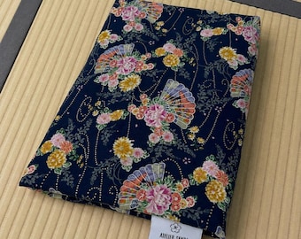 May include: A folded piece of dark navy blue fabric featuring a repeating pattern of colorful pink, yellow, and white flowers interspersed with decorative fans and thin gold dotted lines. A white rectangular tag reads ATELIER SANBA 100% Cotton Handmade in USA www.ateliersanba.com.