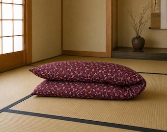 May include: A folded rectangular floor mattress featuring a deep burgundy fabric base with a repeating pattern of small, delicate flowers in shades of light blue, white, and orange. The mattress is thick, soft, and rests flat on the floor surface.