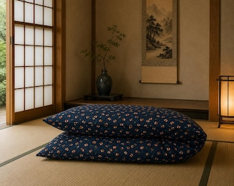 May include: A rectangular floor cushion featuring a dark blue fabric base with a repeating pattern of small, light-colored floral motifs. The cushion is folded in half, resting on a woven straw mat surface in a room with sliding doors.