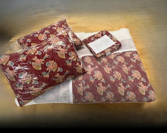 May include: A bedding set featuring a deep red fabric with a repeating pattern of gold and blue fans and floral motifs. The set includes a quilted comforter, a pillow in a clear plastic bag, and a folded fabric square with a white product label.