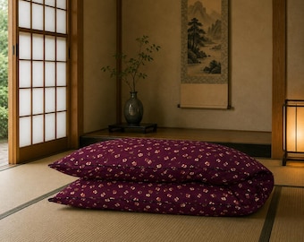 May include: A rectangular floor cushion featuring a deep burgundy fabric with a repeating pattern of small, light-colored floral motifs. The cushion is folded in half, creating two stacked layers, and is placed on a light-colored woven floor mat.