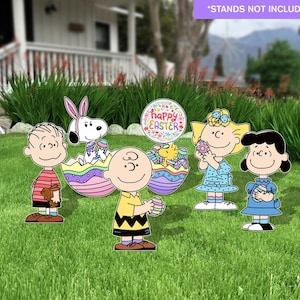 May include: A collection of colorful Easter yard decorations featuring Peanuts characters. The decorations include Charlie Brown, Snoopy, Lucy, and Sally, along with Easter eggs and a sign that says "Happy Easter". The decorations are set on a green lawn.