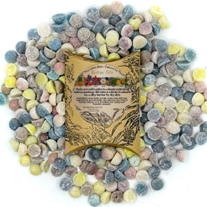 May include: A close-up of a variety of colorful, round, and half-round lotion bars, scattered on a white background. The lotion bars are labeled "Tiny Lotion Bars Colored by Plants Butter Bits".