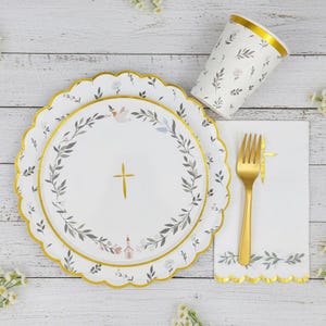 May include: A set of white paper party supplies featuring a gold cross and a delicate gray leaf wreath pattern. The set includes a scalloped-edge dinner plate, a smaller salad plate, a paper cup with a gold rim, a white napkin, and a gold plastic fork.