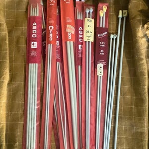 Puede incluir: Un conjunto de agujas de tejer de varios tamaños, empaquetadas en fundas de plástico rojas y transparentes. Las agujas son de color plateado, con tamaños que van desde 3,2 mm hasta 3,75 mm. Algunos paquetes muestran la marca "AERO" y una longitud de 30 cm.