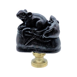 May include: A dark brown lamp finial featuring two rats atop a decorative base. The rats are sculpted in a detailed, realistic style. The base is a dark brown color, and the finial has a brass-colored metal base.