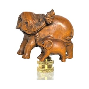 May include: A wooden lamp finial featuring a carved mother elephant with a baby elephant. The elephants are a warm brown color and sit atop a brass-colored base. The finial is designed to be screwed onto a lamp.