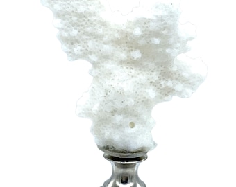 May include: A white coral lamp finial with a silver-colored metal base. The coral has a textured, porous surface. The finial is designed to top a lamp and add a decorative touch.