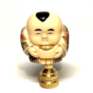 Peut inclure: Figurine ivoire détaillée d'une figurine souriante et potelée avec un accent de cheveux noirs. La figurine tient un objet doré et est montée sur une base en laiton. La figurine a des vêtements détaillés et est un objet décoratif.