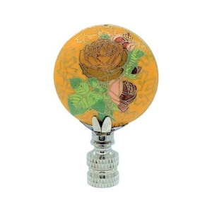 Puede incluir: Un remate de lámpara decorativo con un diseño floral. El remate presenta una parte superior redonda y amarilla con una ilustración detallada de rosas en tonos marrón, rosa y verde. La base es de metal plateado con un diseño texturizado.