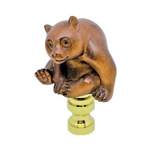 May include: A brown bear figurine sits atop a gold-colored base. The bear is sculpted with detailed fur and features, posed in a seated position. The base has a decorative, hourglass shape. The figurine is set against a white background.