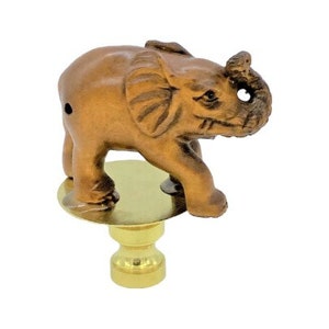 May include: A bronze-colored elephant figurine atop a brass-colored lamp finial. The elephant has detailed features, including large ears and a raised trunk. The finial has a round base and a decorative, tiered stem.