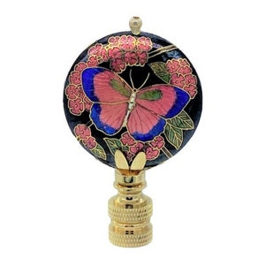 Puede incluir: Un remate de lámpara decorativo con un diseño de mariposa. El remate tiene un fondo negro con flores rosas y una mariposa con alas rosas, azules y verdes. La base es dorada.