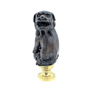 May include: A detailed sculpture of a guardian lion, featuring a dark, weathered finish. The lion sits atop a gold-colored pedestal. The sculpture has intricate details, showcasing the lion's fierce expression and fur.