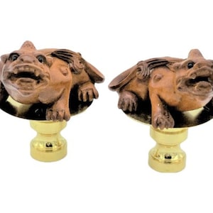 May include: Two brown gargoyle finials with gold-colored bases. The gargoyles have detailed features, including open mouths and wings. The finials are likely for a curtain rod or similar decorative use.