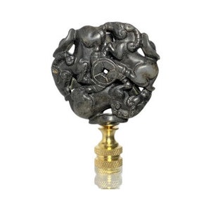 May include: A detailed lamp finial with a dark gray, intricately carved top featuring a circular design with figures. The finial is mounted on a gold-colored base with a textured pattern, adding a touch of elegance.