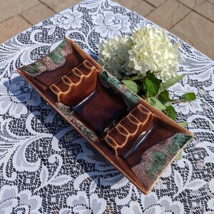 May include: A brown and green ceramic ashtray with three compartments. The ashtray has a mottled glaze and is decorated with a swirl pattern.