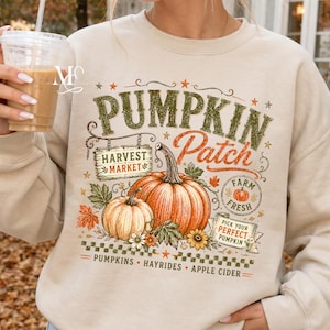 May include: A beige long-sleeve sweatshirt featuring a graphic print with the text PUMPKIN PATCH, HARVEST MARKET, FARM FRESH, and PICK YOUR PERFECT PUMPKIN. The design includes illustrations of orange pumpkins, autumn leaves, and flowers.