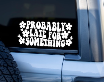 May include: White vinyl sticker with the text "PROBABLY LATE FOR SOMETHING" in a retro font, decorated with flower and star shapes. The sticker is on the rear window of a white vehicle, with a beach and palm tree in the background.