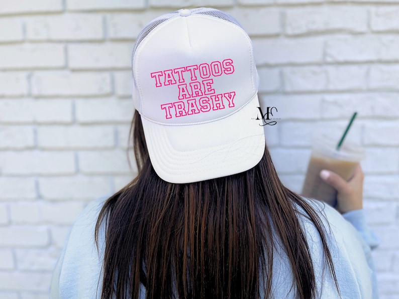 May include: White trucker hat with a pink outline of the text "Tattoos Are Trashy" on the front.