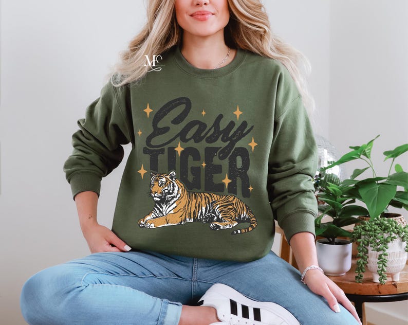 K&ouml;nnte beinhalten: Ein gr&uuml;ner Pullover mit dem Text "Easy Tiger" und einem Comic-Tiger, der auf der Vorderseite aufgedruckt ist. Der Tiger ist orange und schwarz mit wei&szlig;em Hintergrund.