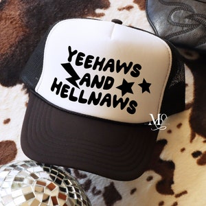 May include: White trucker hat with a black mesh back. The front of the hat has black text that reads "Yeehaws and Hellnaws" with a lightning bolt and two stars.