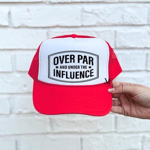 May include: Red and white trucker hat with a black and white graphic that says "Over Par and Under the Influence".