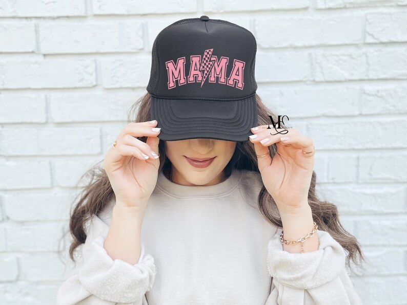 May include: Black trucker hat with a pink checkered lightning bolt and the word "MAMA" in pink letters.