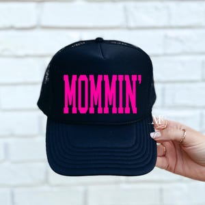 Puede incluir: Gorra de camionero negra con un gr&aacute;fico rosa "MOMMIN'".