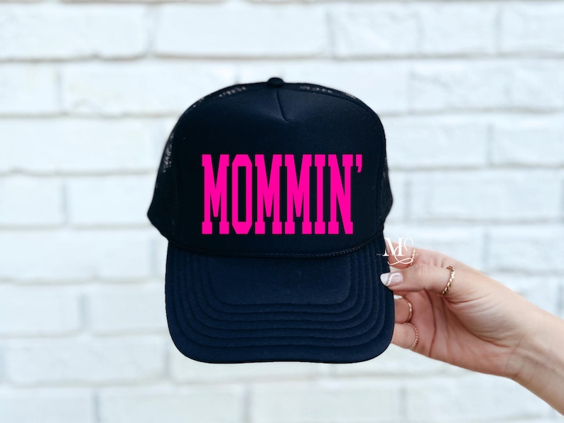 Puede incluir: Gorra de camionero negra con un gr&aacute;fico rosa "MOMMIN'".