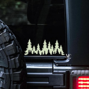 May include: A black car with a white silhouette of a forest on the back window. The car has a spare tire on the back.