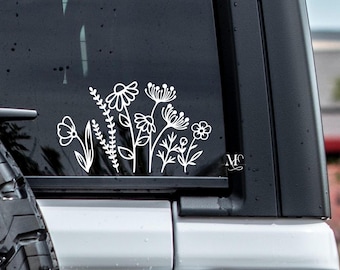 May include: White vinyl decal of a cluster of stylized flowers and leaves on a black car window. The decal is a simple line drawing with no color.