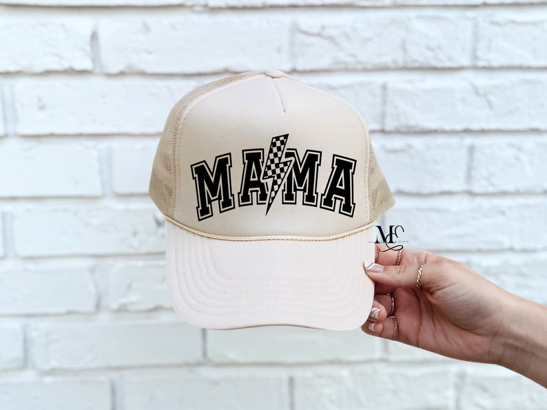 May include: A beige trucker hat with a black and white checkered lightning bolt and the word "MAMA" in black block letters.