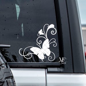 May include: White butterfly decal with intricate wing details and swirling vine accents. The decal is applied to a vehicle window, showcasing a delicate and artistic design. Includes the initials "MS" in a cursive font.
