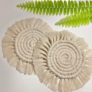 Pode incluir: Dois  copos de croch&ecirc; branco com franjas. Os copos s&atilde;o redondos e t&ecirc;m um padr&atilde;o circular no centro.