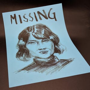 May include: A blue poster with the word "MISSING" written in brown ink at the top. A brown ink drawing of a woman with short brown hair is in the center of the poster.