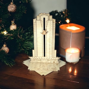 Puede incluir: Un calendario de adviento de madera con forma de rascacielos con 24 ventanas numeradas. Las ventanas están abiertas para revelar una pequeña figura de madera dentro de cada una. El calendario está sobre una mesa de madera.