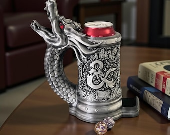 May include: A silver-colored dragon-shaped beverage can holder featuring an embossed Dungeons & Dragons ampersand logo, intricate castle and dragon relief carvings, and a red-rimmed can inside, accompanied by two multi-sided gaming dice.