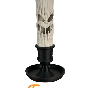 May include: A white candle with a carved face, sitting in a black candlestick. The candle is shaped like a melting face with a wide mouth and two eyes. The candlestick has a round base and a tall, slender stem. "Face 1" is written below the candle.