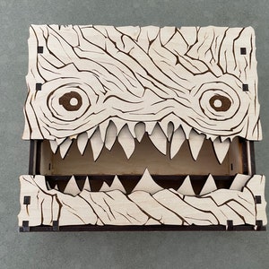 May include: A wooden box with a monster face design. The box has a hinged lid and a compartment inside. The monster face has two eyes, a mouth with sharp teeth, and a textured surface.