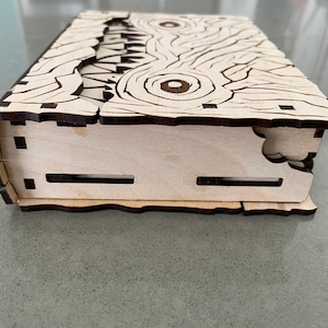 May include: A wooden box with a carved design of a monster's face. The box is closed and the lid is slightly ajar.