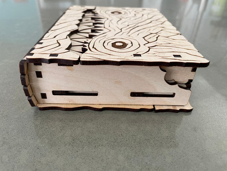 May include: A wooden box with a carved design of a monster's face. The box is closed and the lid is slightly ajar.