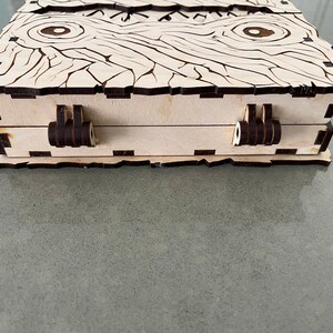 May include: A wooden box with a decorative wood grain pattern and two black hinges. The box has a light wood finish and is closed.