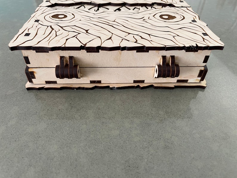 May include: A wooden box with a decorative wood grain pattern and two black hinges. The box has a light wood finish and is closed.