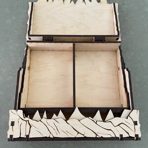 May include: A wooden box with a hinged lid and two compartments. The box is decorated with a design of jagged peaks, resembling a mountain range.