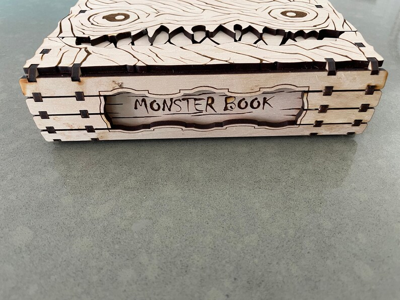 May include: A wooden box with a carved monster face on the front. The box is labeled "Monster Book".