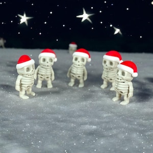 Puede incluir: Cinco figuritas de esqueleto blancas con gorros de Papá Noel rojos están de pie sobre una superficie blanca con un fondo de cielo estrellado.